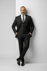 Man wearing black peak lapel three-piece suit with tailored fit for formal occasions.